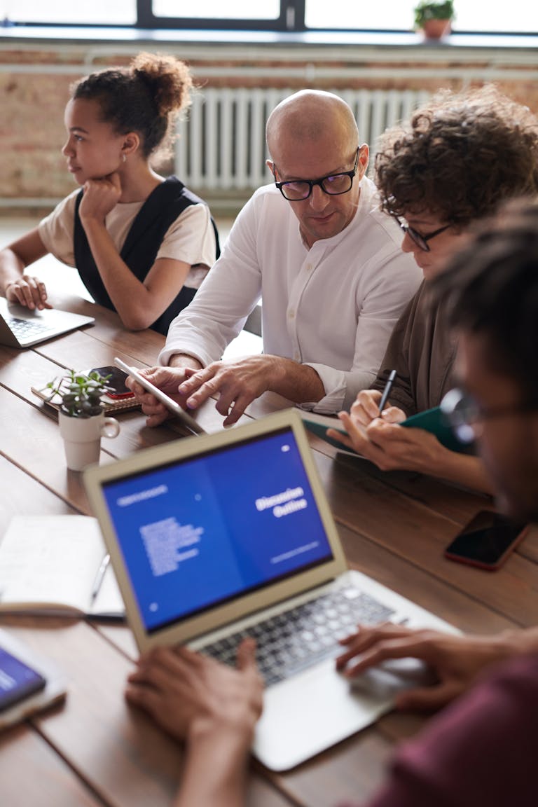 Diverse team engaged in a collaborative business meeting around a wooden table with laptops.